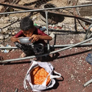 طفل فلسطيني يتناول وجبة بمخيم النصيرات وسط قطاع غزة (الفرنسية)
