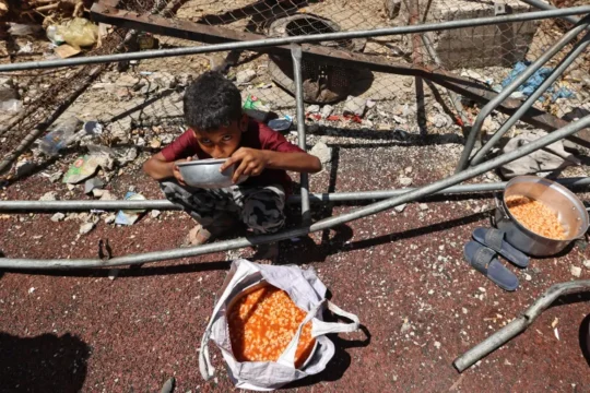 طفل فلسطيني يتناول وجبة بمخيم النصيرات وسط قطاع غزة (الفرنسية)